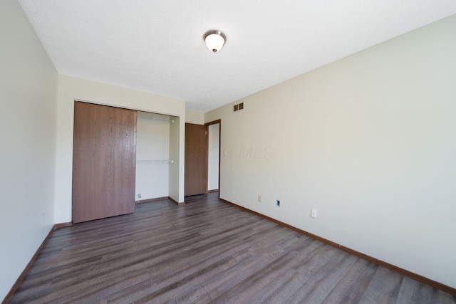 unfurnished bedroom featuring baseboards, visible vents, dark wood finished floors, and a closet
