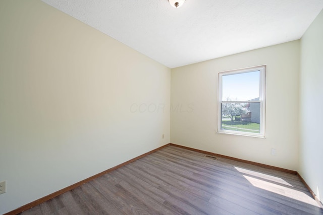 spare room with baseboards, wood finished floors, and visible vents