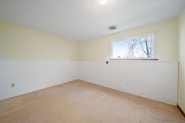 unfurnished room with light colored carpet, a textured ceiling, a wainscoted wall, and visible vents