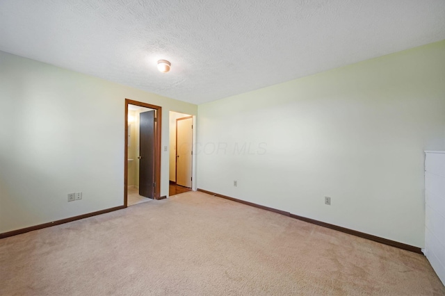spare room with baseboards, a textured ceiling, and light colored carpet