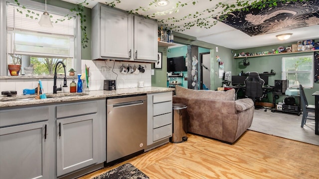kitchen featuring gray cabinets, backsplash, stainless steel dishwasher, a sink, and open floor plan