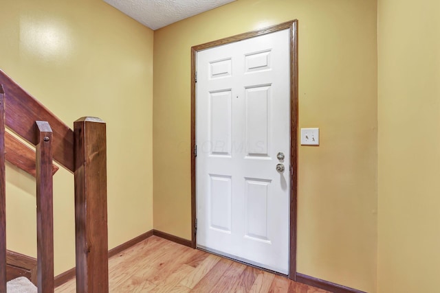 foyer entrance with baseboards, a textured ceiling, and light wood finished floors