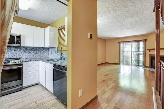 kitchen with a textured ceiling, white cabinets, a sink, light wood finished floors, and appliances with stainless steel finishes