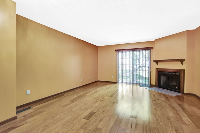 unfurnished living room with baseboards, visible vents, a fireplace with flush hearth, and light wood-style flooring