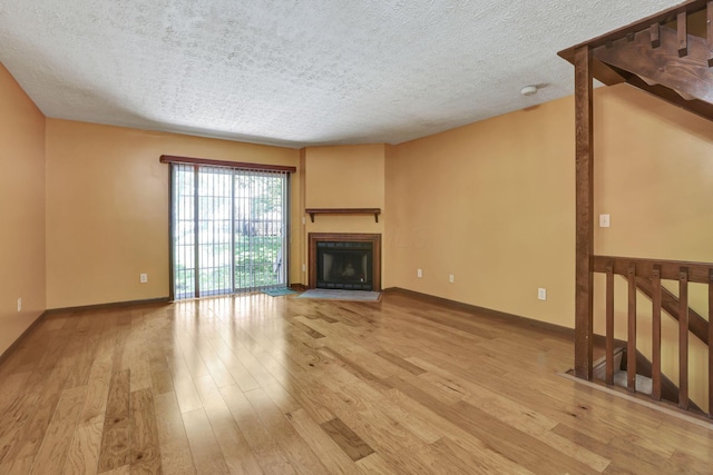 unfurnished living room with light wood-style floors, baseboards, a fireplace, and a textured ceiling