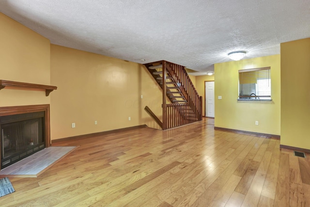 unfurnished living room with stairs, wood finished floors, baseboards, a textured ceiling, and a fireplace with flush hearth