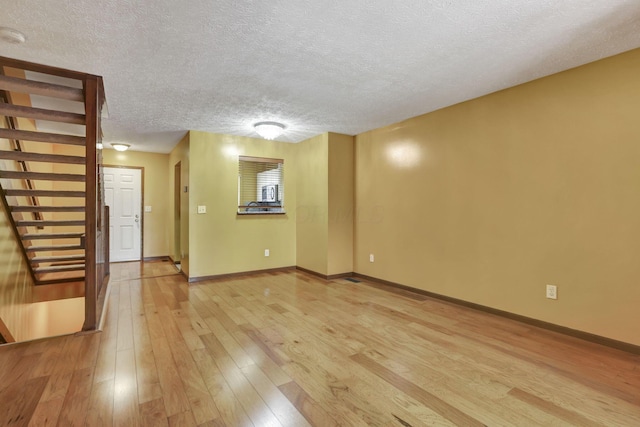 unfurnished living room featuring baseboards, light wood finished floors, and a textured ceiling
