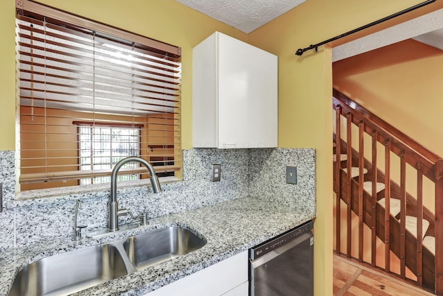 kitchen with white cabinets, decorative backsplash, a sink, and dishwasher
