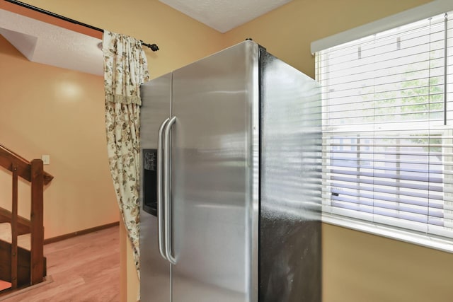 kitchen with a textured ceiling, baseboards, stainless steel fridge with ice dispenser, and light wood-style floors