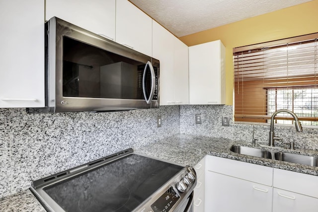 kitchen featuring white cabinetry, tasteful backsplash, light stone counters, a sink, and appliances with stainless steel finishes