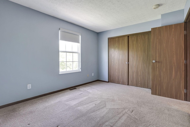 unfurnished bedroom featuring carpet flooring, a textured ceiling, baseboards, visible vents, and a closet