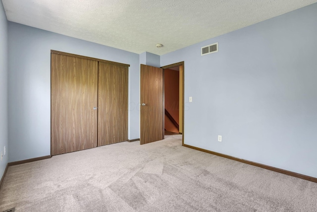 unfurnished bedroom featuring visible vents, a closet, baseboards, a textured ceiling, and carpet flooring