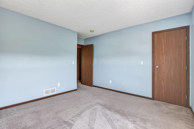 spare room featuring baseboards, carpet, a textured ceiling, and visible vents