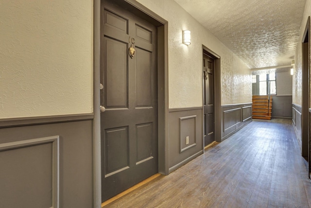 interior space featuring a textured ceiling, a textured wall, wood finished floors, and a wainscoted wall
