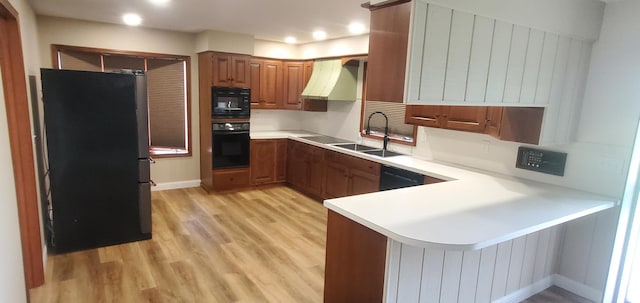 kitchen with brown cabinetry, light countertops, black appliances, light wood finished floors, and a peninsula
