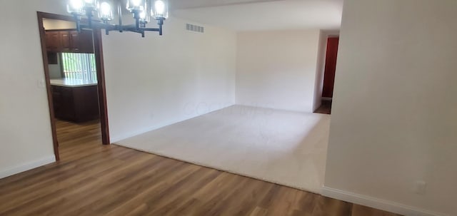 empty room featuring baseboards, visible vents, wood finished floors, and an inviting chandelier