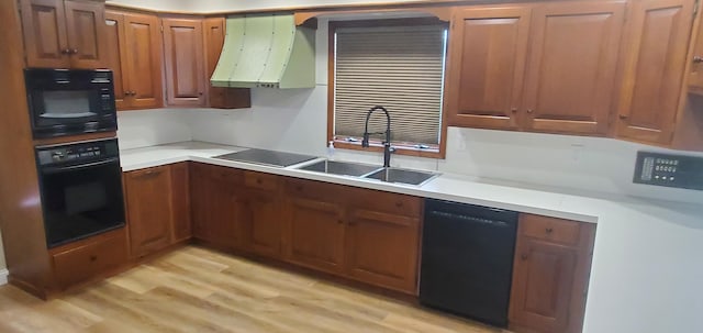 kitchen with brown cabinetry, light wood-style floors, light countertops, a sink, and black appliances