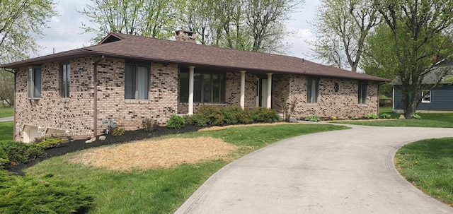 ranch-style home with brick siding, a chimney, a shingled roof, and a front lawn