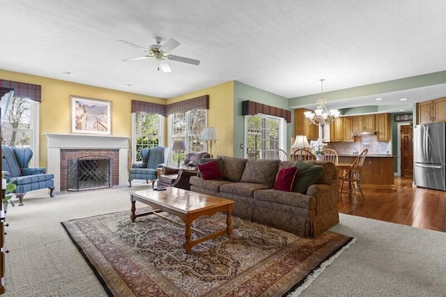 living area featuring plenty of natural light, a brick fireplace, and ceiling fan with notable chandelier