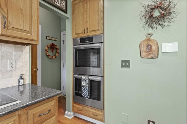 kitchen featuring decorative backsplash, double oven, black electric stovetop, dark stone counters, and light wood-style flooring