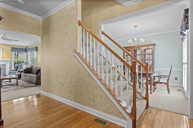 stairs featuring crown molding, ceiling fan with notable chandelier, baseboards, visible vents, and hardwood / wood-style flooring