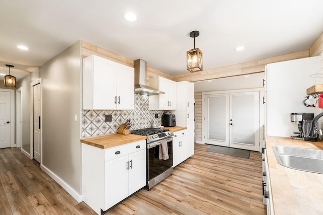 kitchen with stainless steel gas range oven, wall chimney range hood, light wood-style flooring, a sink, and wood counters