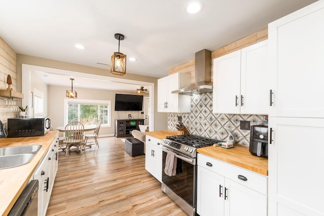 kitchen with appliances with stainless steel finishes, a sink, wooden counters, wall chimney exhaust hood, and tasteful backsplash
