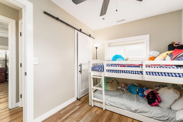 bedroom featuring a barn door, light wood-style floors, a ceiling fan, baseboards, and visible vents