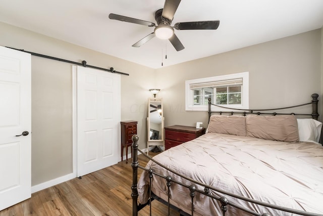 bedroom featuring baseboards, a barn door, ceiling fan, and wood finished floors