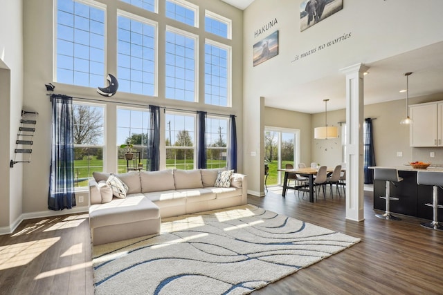 living room featuring baseboards, dark wood-style floors, ornate columns, and a towering ceiling
