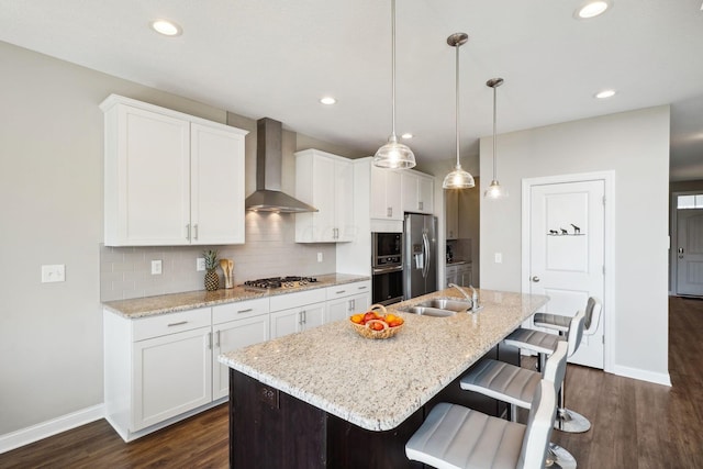 kitchen with baseboards, appliances with stainless steel finishes, an island with sink, and wall chimney exhaust hood