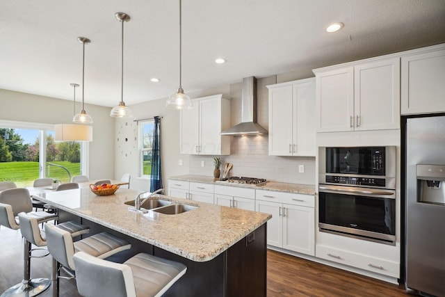 kitchen with wall chimney exhaust hood, white cabinetry, tasteful backsplash, a sink, and appliances with stainless steel finishes