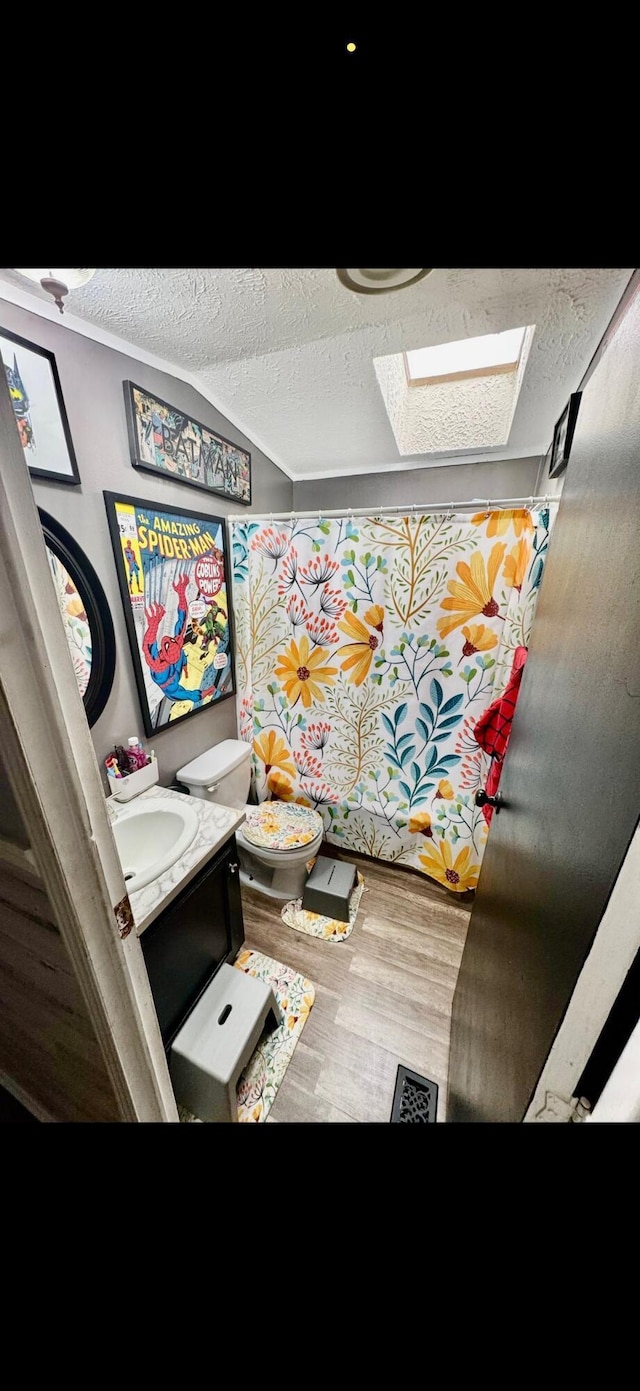 full bath with toilet, a textured ceiling, wood finished floors, and vanity