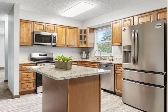 2257 Jarrow Dr, Hilliard, OH 43026 - kitchen featuring stainless steel appliances, a textured ceiling, light wood finished floors, brown cabinetry, and light stone counters