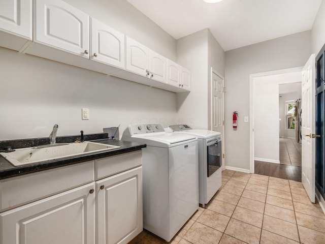 washroom with light tile patterned flooring, baseboards, washer and clothes dryer, a sink, and cabinet space