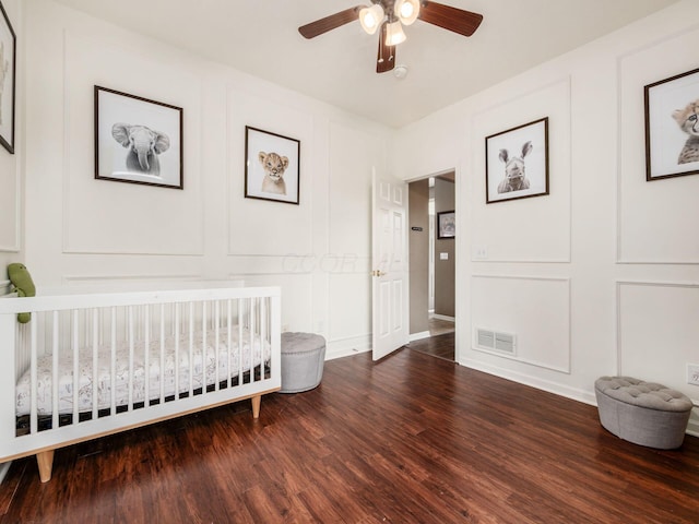 bedroom featuring a nursery area, a decorative wall, wood finished floors, and visible vents