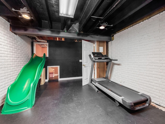 exercise room with baseboards and brick wall