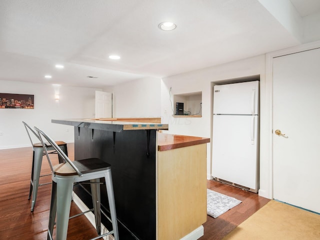 kitchen featuring wooden counters, freestanding refrigerator, a breakfast bar, recessed lighting, and dark wood-type flooring