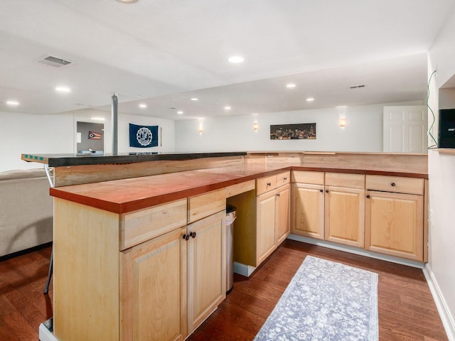 kitchen featuring light brown cabinetry, a breakfast bar area, butcher block countertops, open floor plan, and dark wood-style floors