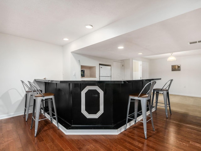 kitchen with freestanding refrigerator, a breakfast bar, wood finished floors, and visible vents