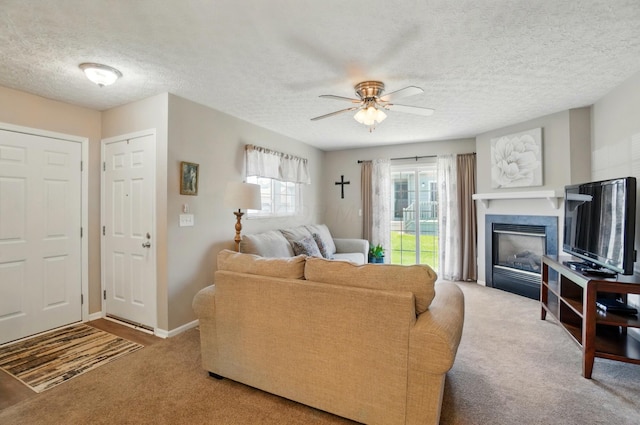 living room featuring ceiling fan, a textured ceiling, carpet floors, baseboards, and a glass covered fireplace