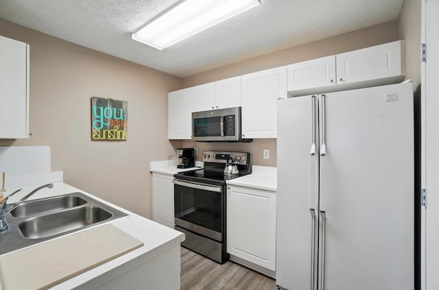 kitchen with a sink, light countertops, stainless steel appliances, white cabinetry, and light wood-type flooring