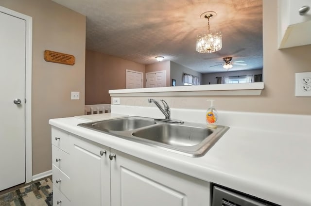 kitchen with white cabinets, a sink, dishwasher, light countertops, and ceiling fan with notable chandelier