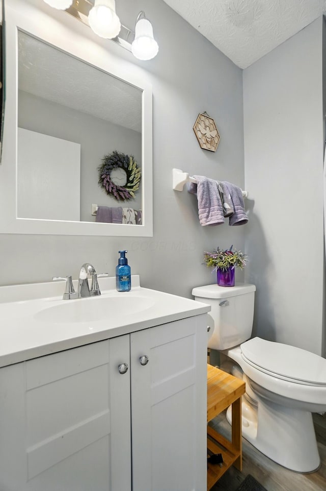 half bathroom featuring vanity, a textured ceiling, wood finished floors, and toilet