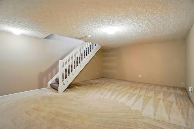 finished basement featuring carpet floors, a textured ceiling, baseboards, visible vents, and stairway