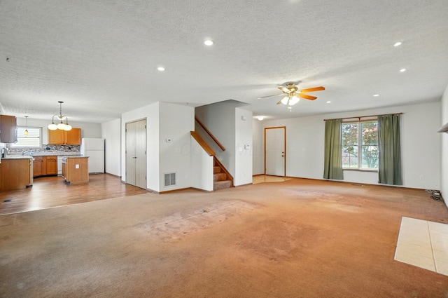 unfurnished living room featuring light colored carpet, a textured ceiling, ceiling fan with notable chandelier, recessed lighting, and visible vents