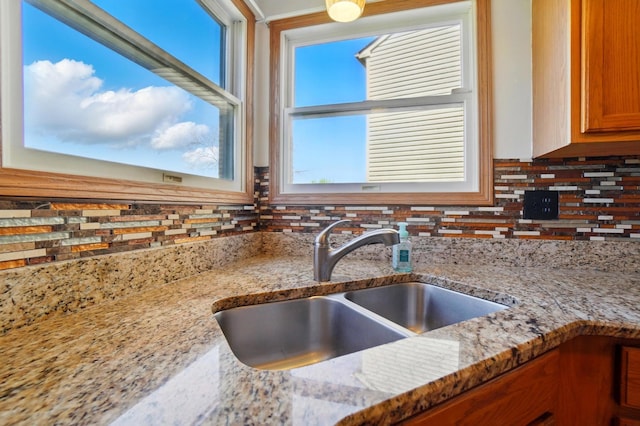 kitchen featuring brown cabinetry, light stone counters, decorative backsplash, and a sink