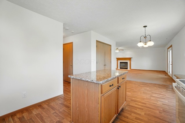 kitchen with a kitchen island, pendant lighting, open floor plan, a glass covered fireplace, and light wood-style flooring