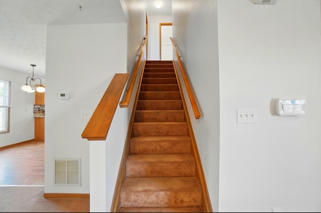 stairs with a textured ceiling, visible vents, carpet floors, baseboards, and a notable chandelier