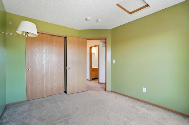 unfurnished bedroom with a closet, baseboards, attic access, a textured ceiling, and carpet flooring